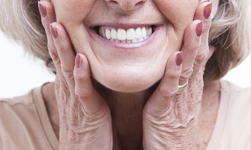 older woman holding her face as she smiles with dentures