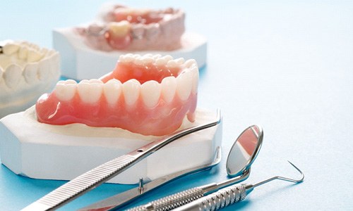 A closeup of a denture next to dental tools against a blue background