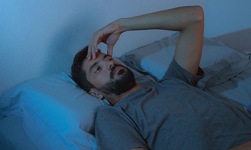 Man laying awake with hand on his head looking up at the ceiling