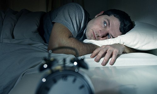 Man lying awake with clock next to his bed