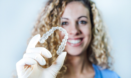 A young dental hygienist wearing gloves and holding a clear aligner meant for Invisalign in Tysons
