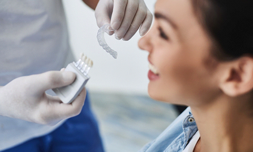 A dentist holding a shade guide and Invisalign aligner as a patient smile in preparation for her first fitting