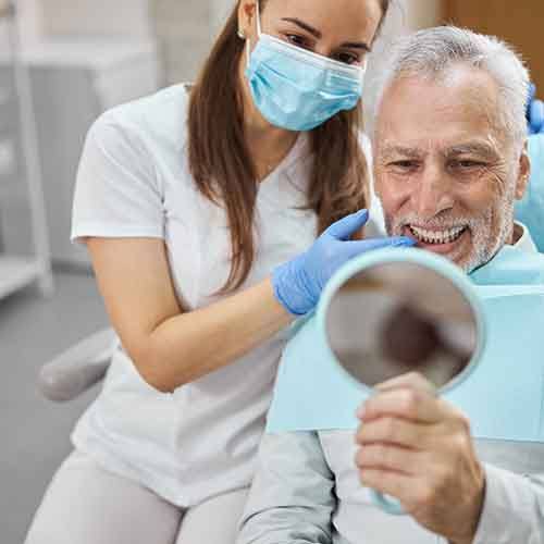 a man smiling and looking in a handheld mirror at the dental office