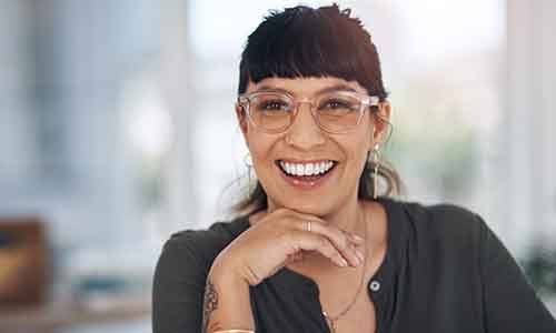 a smiling woman with glasses resting her chin on her hand