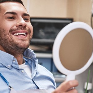 a man smiling and looking into a handheld mirror
