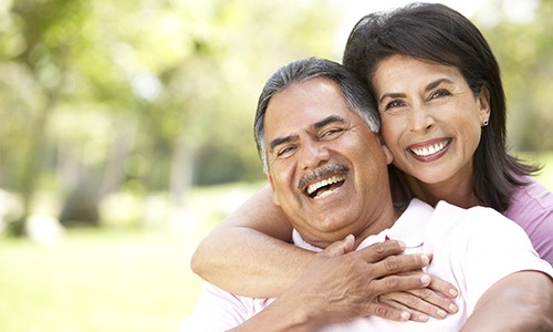 Middle-aged couple smiling outside with arms around each other