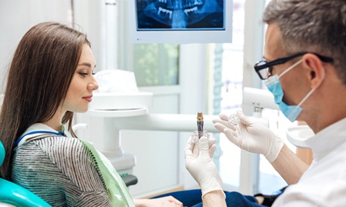 A male dentist showing a female patient what a dental implant looks like to replace a missing tooth