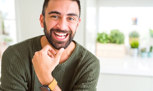 A gentleman wearing a green sweater and watch, smiling about his new and improved look thanks to a recent smile makeover