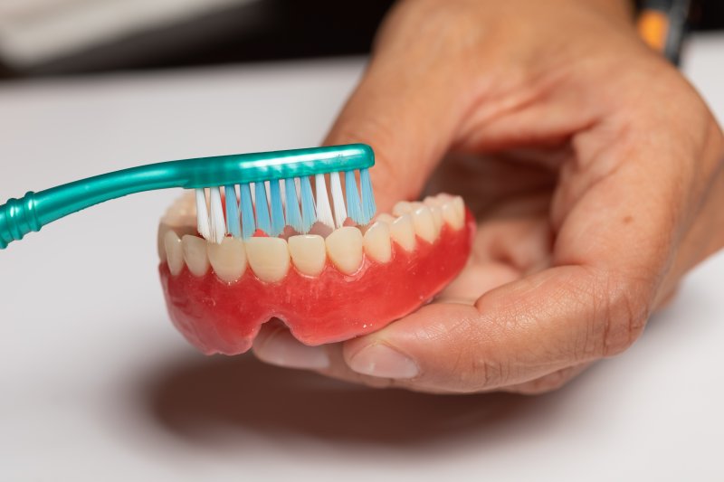 person cleaning dentures with toothbrush